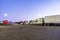 Different big rig semi trucks with semi trailers standing in row on truck stop parking lot at evening time for rest of drivers and