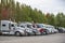 Different big rigs semi trucks standing in row on parking lot with trees on the background