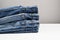 Different classic jeans. A stack of folded jeans on white table with copy space. Basic wardrobe concept