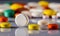 Different colored pills and tablets scattered on a glossy reflective surface. Close up of white, yellow, brown, green