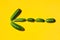 Different cucumbers on a yellow background form an arrow symbol