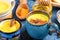 Different cups with golden turmeric milk, curcuma powder and honey on blue textured backdrop. Close-up, selective focus