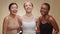 Different female beauty. Three happy diverse young women embracing together and laughing to camera, beige background