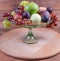 Different fruits in glass fruit vase on wooden serving board