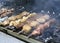 Different kinds of meat are roasted on skewers on coals during a street fair.