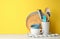 Different kitchen utensils on white table against yellow background