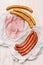 Different long sausages and ham in a crumpled paper packaging on rustic wooden background, top view