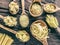 Different pasta types in wooden spoons on the table. Top view.