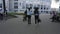 Different people wander along grey paved road past building