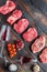 Different raw beef steaks with seasonings and red wine in bottle and glass  on old wooden dark planks top view with space for text