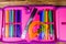 Different school stationeries pens, pencils, felt tip pens, ruler and protractor in a pink pencil box. Top view