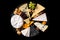 Different sorts of cheese set. Cheese platter with various cheese, with grapes, nuts, cheese knife and spices, black tiled