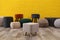 Different stylish poufs and ottomans near yellow brick wall