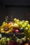 Different summer fruits in an iron bowl with a sunflower on a wooden background, close up