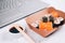 Different sushi rolls with salmon in delivery paper box on white marble table background with laptop - futomaki, uramaki