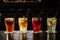 Different types of summer drinks in glasses, cubes of ice and slice of fruits on dark wiooden table