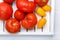 Different varieties of tomatoes on a white tray. Colorful red and yellow fresh ripe tomatoes. Top view