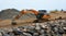 Digger moving large boulders on construction site.