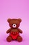Digital 3D render of a cute romantic brown teddy bear figure with a heart on a pink background
