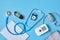 Digital blood pressure monitor, glucometer, stethoscope, notepad and alarm clock on blue background top view