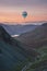 Digital composite image of hot air balloons over Stunning colorful landscape image of view down Honister Pass to Buttermere from