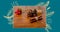 Digital composite of tied cinnamon sticks by pine cones and cherries on table over blue background