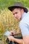 Digital farm. Portrait of farmer seating in gold wheat field and scrolling on tablet. Young man wearing cowboy hat in