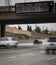 Digital freeway sign at overpass with message stating â€œStop The Spread ,Stay Home, Save Livesâ€ and traffic blurred