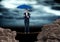 Digital image of businesswoman standing on rope amidst rocks holding blue umbrella against cloudy sk