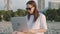 Digital nomad woman in sunglasses working with laptop sits on the beach by the sea during sunset. Female freelancer work