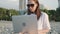 Digital nomad woman in sunglasses working with laptop sits on the beach by the sea during sunset. Female freelancer work