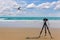Digital professional camera stand on tripod photographing sea, Passenger plane flying over beautiful blue ocean .