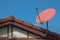 Digital satellite television receiving dish setting on top of house roof with blue sky in background.