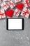 Digital tablet blank screen with gift box and hearts decor on gray cement table. Top view. Valentines Day concept background