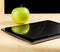 Digital tablet pc and green apple in front of blackboard on wood table