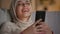 Digital tv in pocket. Young cheerful muslim woman in hijab watching movie on smartphone and laughing in evening at home