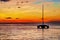 Digitally created watercolor painting of a vibrant sunset with strong orange hues and a silhouetted sailboat
