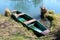 Dilapidated river boat with faded paint secured at local river bank surrounded with calm river water and uncut grass