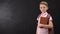 Diligent schoolboy holding textbook, standing near blackboard, education system