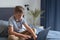 Diligent schoolboy using his laptop for doing homework, sitting on his bed in modern interior. Studying online during