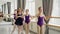 Diligent young ballet-dancers are doing plie and battement tendu while their female teacher is correcting wrong