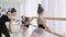 Diligent young ballet-dancers are doing plie and battement tendu while their female teacher is correcting wrong