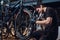 Diligent young mechanic is repairing customer`s bicycle at workplace