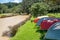 Dinghies and kayaks upturned on grass near beach surrounded by trees