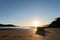 Dinghy sitting on sand at low tide in silhouette backlit by setting sun