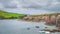 Dingle Lighthouse on the edge of the cliff with green fields in a distance