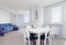 Dining area in white modern apartment with massive dining table and six chairs with window and blue furniture home