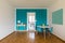 Dining room front view with small desk and turquoise wall. Open door to white kitchen and bright window