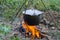 Dinner at the camp. The iron cauldron, blackened by the fire, hangs on a tripod over the fire