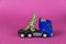 Dinosaur and tractor-trailer against a purple background. Green plastic miniature of a predatory animal. Children`s toy.